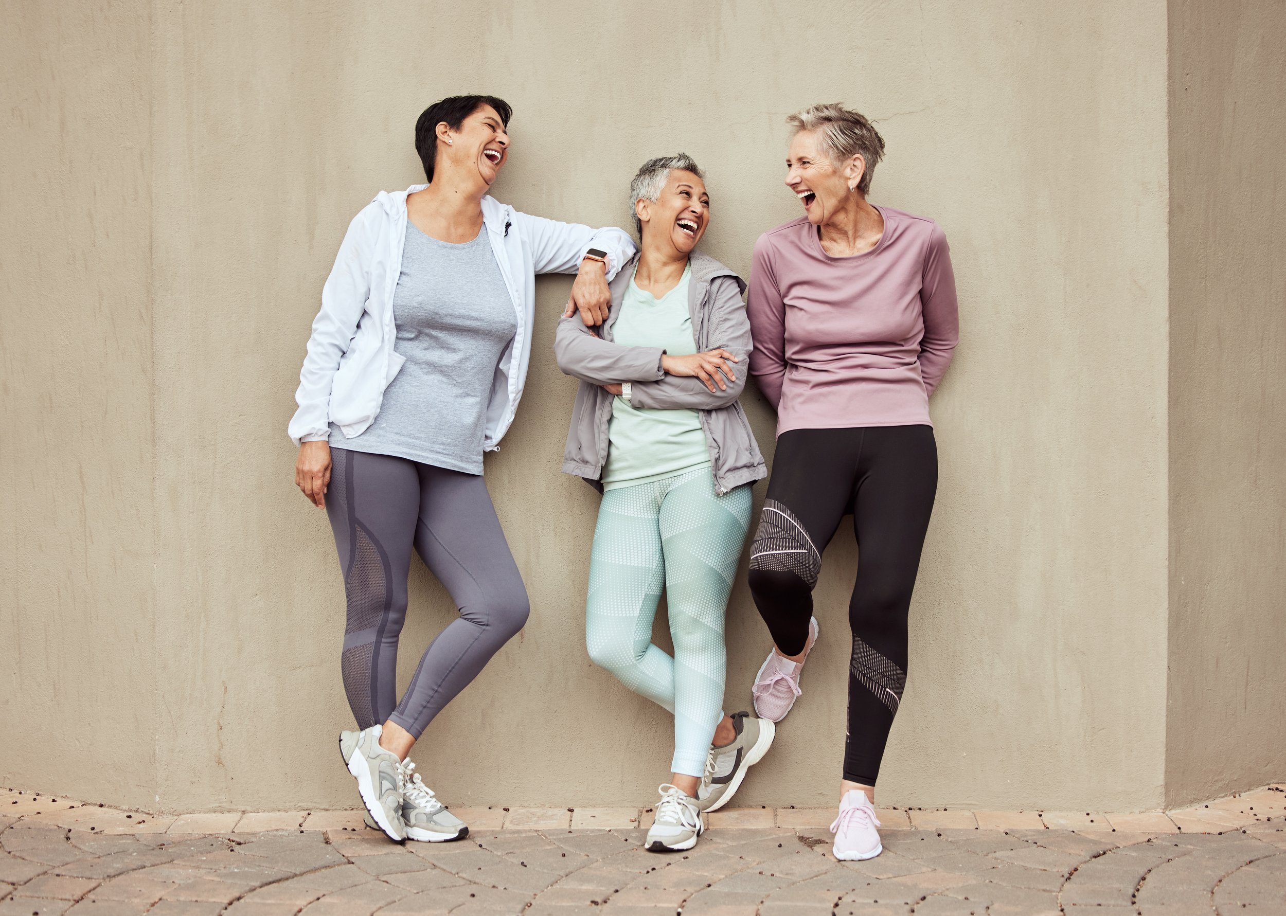 Senior women, exercise and funny with retirement, fitness and wellness, vitality and active lifestyle against wall background. Mature female friends, comedy and training, relax and sports motivation.
