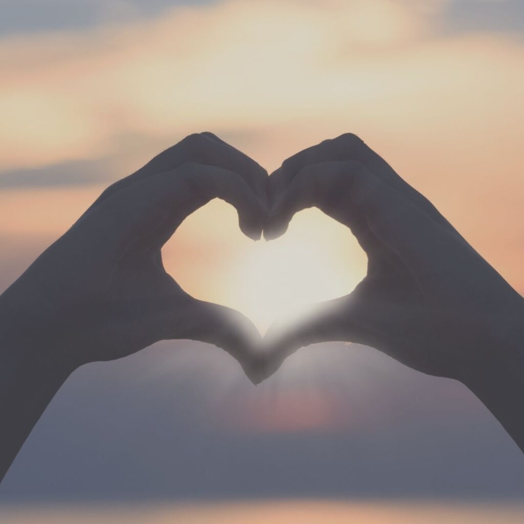 Two hands held in a heart shape over a sunset.